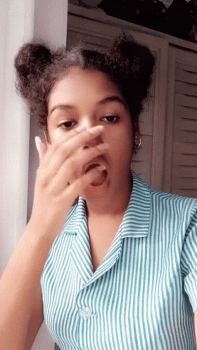 A Young Woman In A Striped Shirt Is Covering Her Face With Her Hand . GIF