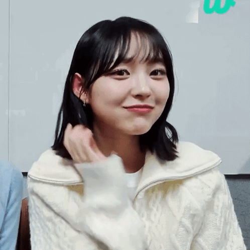 A Young Woman In A White Sweater Is Smiling GIF
