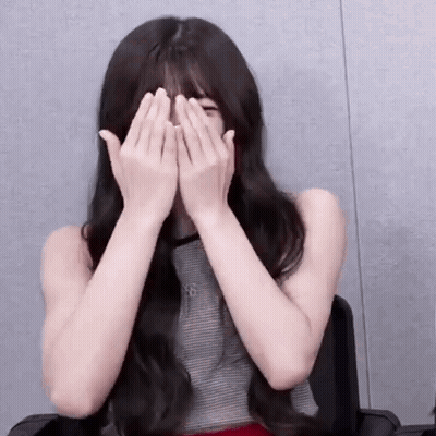 A Young Woman Is Covering Her Face With Her Hands While Sitting In A Chair . GIF