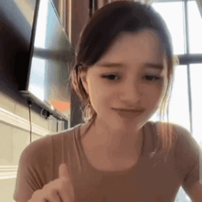A Young Woman Is Giving A Thumbs Up Sign While Sitting At A Table In Front Of A Television . GIF