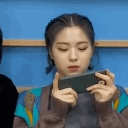 A Young Woman Is Holding A Cell Phone In Her Hands . GIF