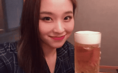 A Young Woman Is Holding A Glass Of Beer And Smiling . GIF