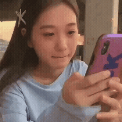 A Young Woman Is Looking At Her Cell Phone While Wearing A Blue Shirt . GIF