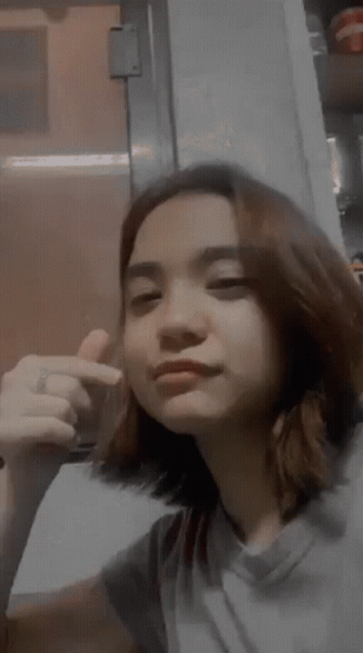 A Young Woman Is Making A Funny Face And Giving A Thumbs Up Sign . GIF