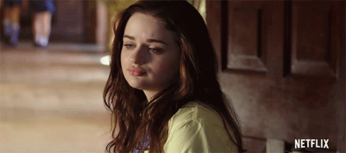 A Young Woman Is Sitting In Front Of A Door Looking At The Camera . GIF