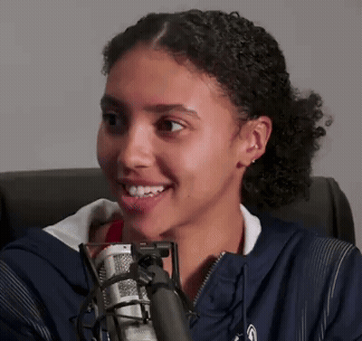 A Young Woman Is Smiling In Front Of A Microphone GIF