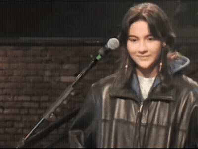 A Young Woman Is Smiling In Front Of A Microphone In A Dark Room . GIF