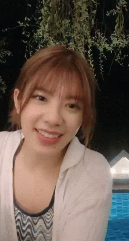 A Young Woman Is Smiling In Front Of A Pool At Night GIF