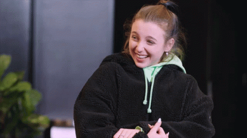 A Young Woman Wearing A Black Jacket And A Green Hoodie Smiles GIF