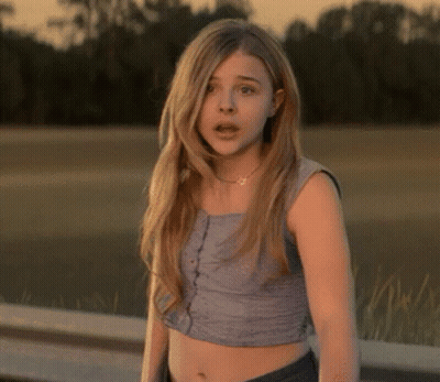 A Young Woman Wearing A Crop Top Stands In Front Of A Body Of Water GIF