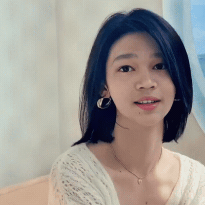 A Young Woman Wearing A Necklace And Earrings Is Smiling GIF