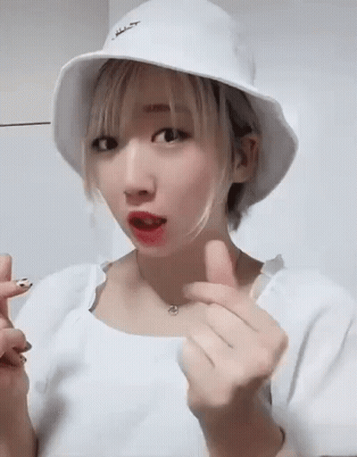 A Young Woman Wearing A White Hat And A White Shirt Is Making A Heart Shape With Her Hands . GIF