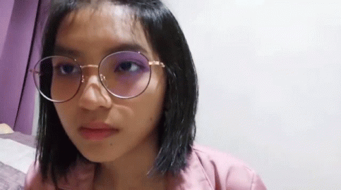 A Young Woman Wearing Glasses And A Pink Shirt Is Making A Funny Face . GIF