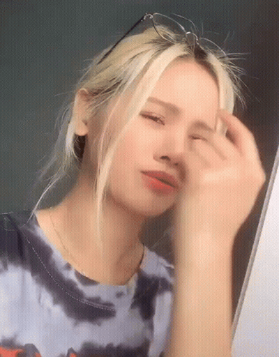 a young woman wearing glasses and a tie dye shirt is looking at herself in the mirror .
