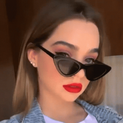 A Young Woman Wearing Sunglasses And Red Lipstick Is Looking At The Camera . GIF