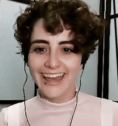 A Young Woman With Curly Hair Is Smiling And Wearing Headphones . GIF