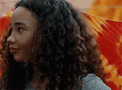 A Young Woman With Curly Hair Is Standing In Front Of A Colorful Wall . GIF