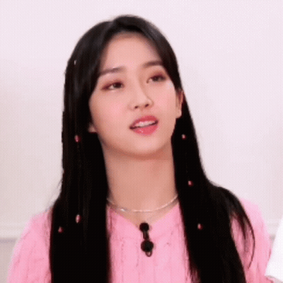 A Young Woman With Long Black Hair Is Wearing A Pink Sweater And Necklace . GIF