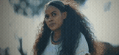 A Young Woman With Long Curly Hair Is Standing In Front Of A Smokey Background . GIF