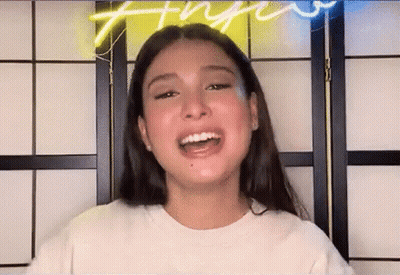 A Young Woman With Long Hair Is Smiling In Front Of A Neon Sign . GIF