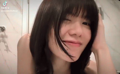 A Young Woman With Short Black Hair Is Making A Funny Face While Holding Her Hair . GIF