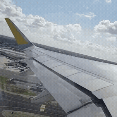 Airplane Wing With Yellow Tail Over Runway GIF