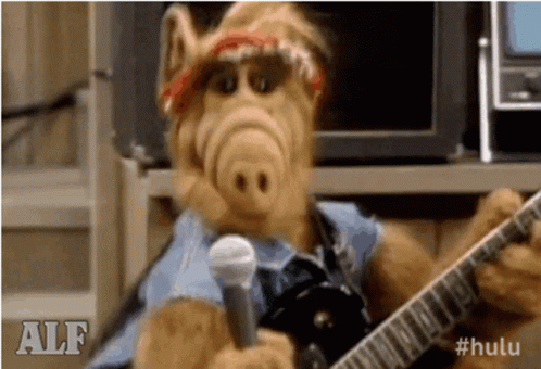 Alf From The Simpsons Is Holding A Guitar And A Microphone . GIF