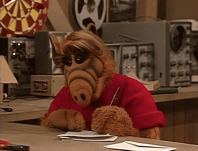 ALF Sitting At Desk With Pen GIF
