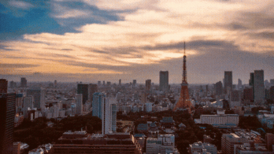 An Aerial View Of A City At Sunset With A Tower In The Foreground GIF