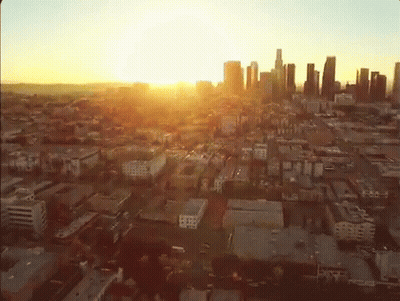 An Aerial View Of A City At Sunset With The Sun Shining Through The Clouds GIF