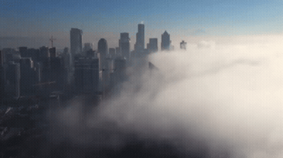 An Aerial View Of A City Skyline Covered In Clouds GIF