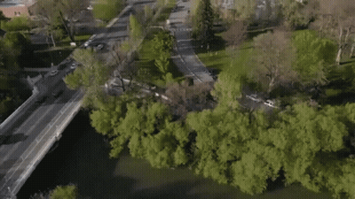 An Aerial View Of A City With A Bridge Over A River Surrounded By Trees . GIF