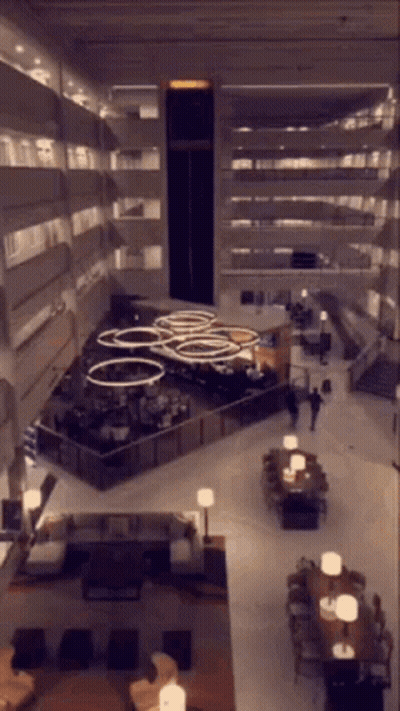 An Aerial View Of A Hotel Lobby With Tables Chairs And Stairs GIF