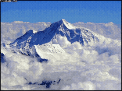 An Aerial View Of A Snowy Mountain Covered In Clouds With Senorgif.com In The Upper Right Corner GIF