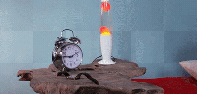 An Alarm Clock Sits On A Table Next To A Lava Lamp And A Watch GIF