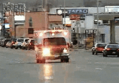 An Ambulance Is Driving Down A Street In Front Of A Tapco GIF