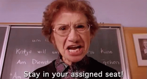 An Angry Teacher Says Stay In Your Assigned Seat In Front Of A Chalkboard GIF