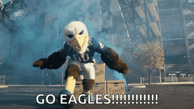 An Eagle Mascot Says Go Eagles In Front Of Boxes Of Fireworks GIF