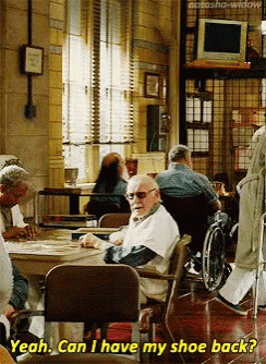 An Elderly Man In A Wheelchair Is Sitting At A Table In A Nursing Home And Asking If He Can Have His Shoe Back GIF