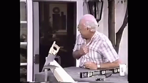 An Elderly Man Is Cutting A Piece Of Wood With A Saw On A Table . GIF