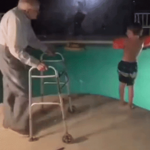 An Elderly Man Is Using A Walker To Help A Young Boy Jump Into A Pool . GIF