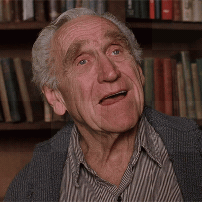 An Elderly Man Making A Funny Face In Front Of Bookshelves GIF