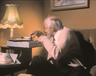 An Elderly Man Sits In A Chair Eating A Pizza GIF
