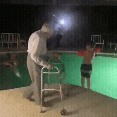An Elderly Man With A Walker Is Helping A Young Boy With A Life Preserver Into A Swimming Pool . GIF