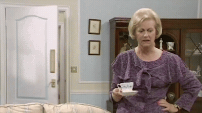 An Elderly Woman In A Purple Dress Is Holding A Cup Of Coffee In A Living Room . GIF