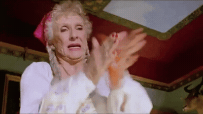 An Elderly Woman In A White Dress Is Clapping Her Hands In A Room . GIF