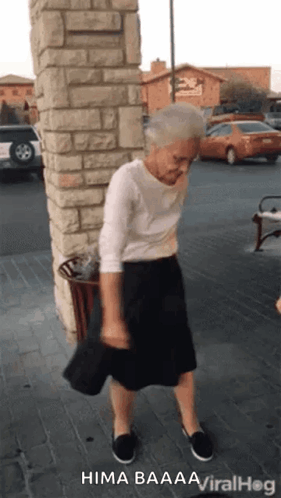 An Elderly Woman In A White Shirt And Black Skirt Is Dancing On The Sidewalk . GIF