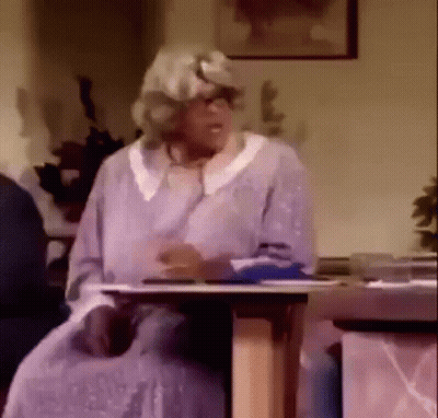 An Elderly Woman In A Wig Is Sitting At A Table . GIF