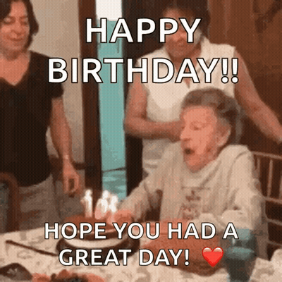 An Elderly Woman Is Blowing Out Candles On A Birthday Cake While Sitting At A Table . GIF