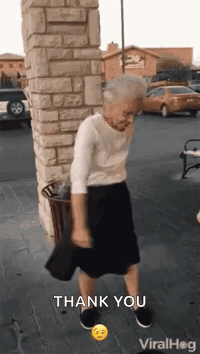 An Elderly Woman Is Dancing In Front Of A Brick Wall In A Parking Lot While Holding A Hat . GIF